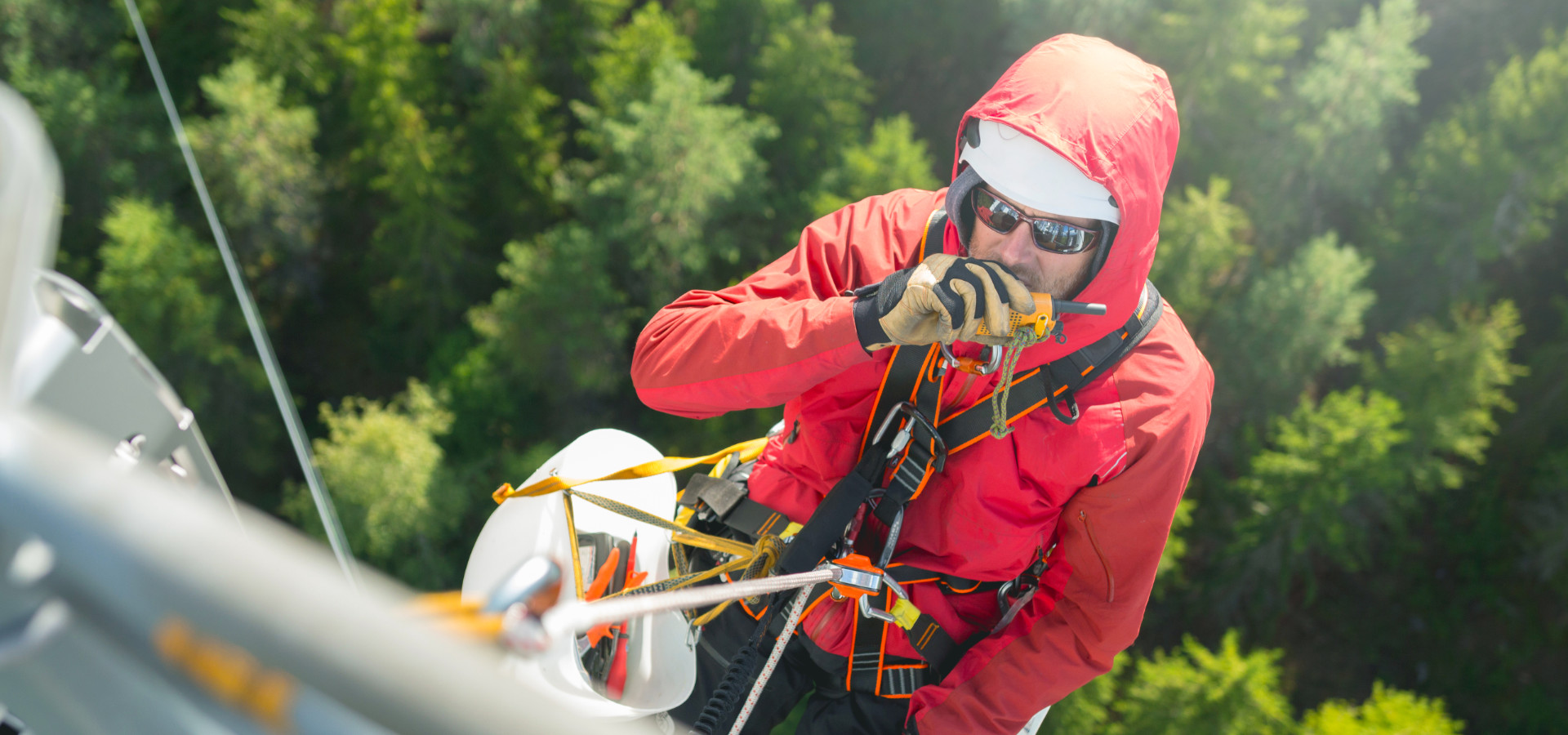 Mann in Schutzkleidung und mit Seilen gesichert arbeitet hoch oben auf einem Mobilfunkmast. Hintergrund: Den Bau neuer Mobilfunkmasten zu fördern – das ist das Unternehmensziel der MIG, damit bestehende Funklöcher in Deutschland beseitigt werden. Denn obwohl die Mobilfunknetze in den letzten Jahren immer weiter ausgebaut wurden, existieren noch immer mehrere tausend Funklöcher, in denen keine mobile und breitbandige Datenübertragung möglich ist. Die aber ist die Voraussetzung dafür, dass Chancengleichheit hergestellt und allen Bürger*innen, Gemeinden und Unternehmen der Anschluss an das Entwicklungspotential und die Zukunftschancen der Digitalisierung möglich ist.